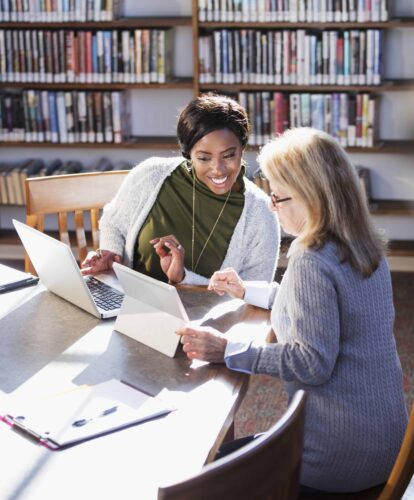 Two women with laptops working together in library