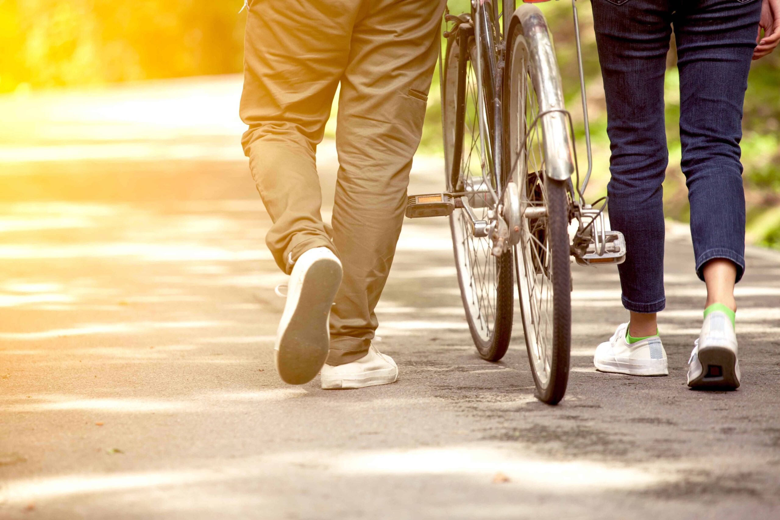 Back view of young couple walking together with bicycle in the garden A student pushing a bicycle